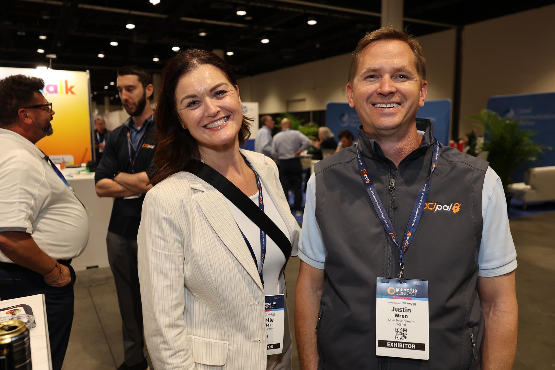 TWO ATTENDEES SMILING AT THE CAMERA IN THE EXPO HALL