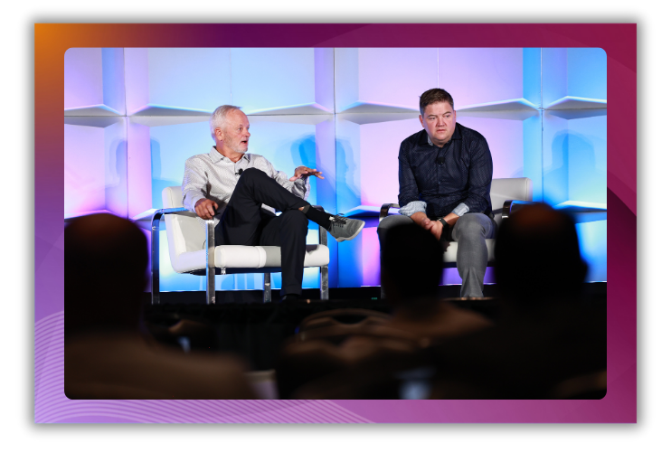 A photo of two men sitting onstage speaking to a crowd