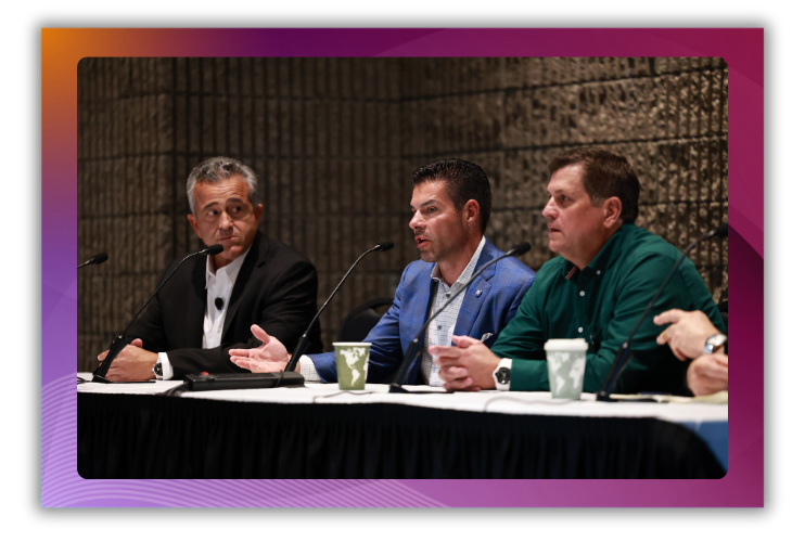 A photo of three men speaking onstage in a conference session