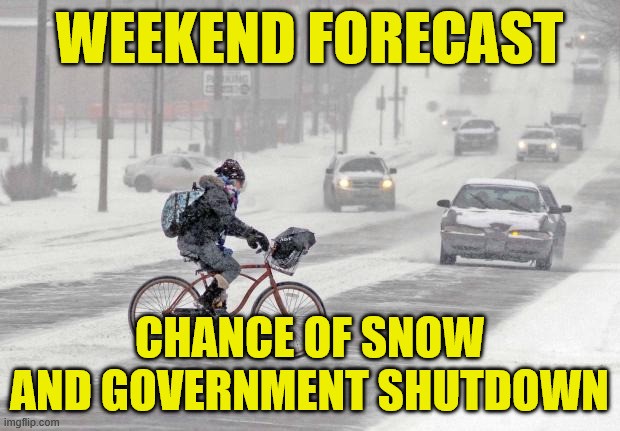 A person bundled up in winter gear riding a bike across a busy snow covered street with cars driving at the person as a snow continues to fall and a storm threatens.