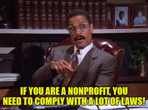A Black man in a brown suit sitting behind a desk in a fancy leather chair and in front of a full shelf of legal textbooks. Meme text reads 'If you are a nonprofit, you need to comply with a lot of laws!'